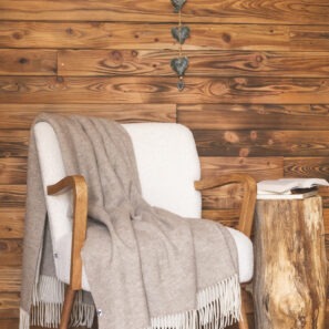 Plaid CÔME à franges drapé sur un fauteuil blanc dans un intérieur en bois