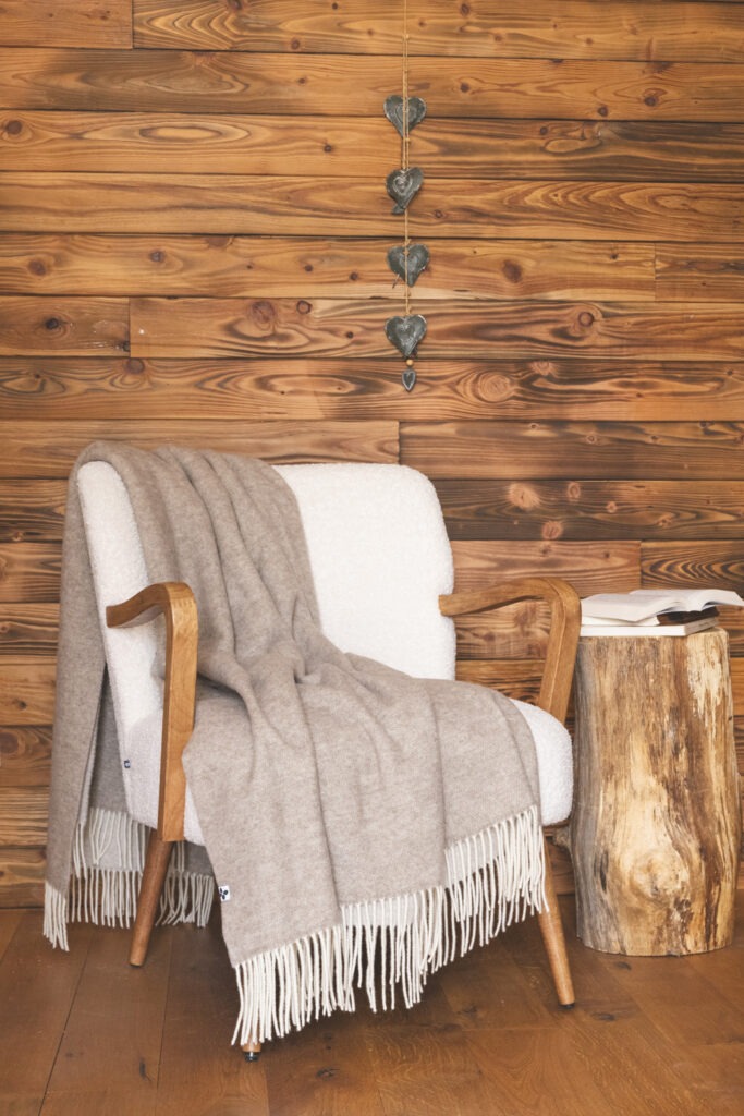 Plaid CÔME à franges drapé sur un fauteuil blanc dans un intérieur en bois