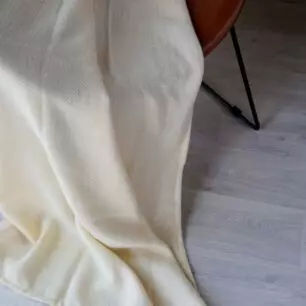 Plaid HANOI Naturale in lana e seta su una poltrona, motivo a spina di pesce visibile