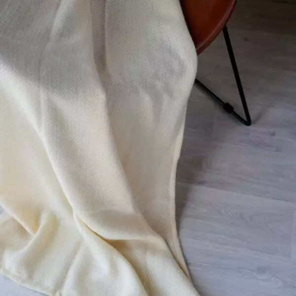 Plaid HANOI Naturale in lana e seta su una poltrona, motivo a spina di pesce visibile